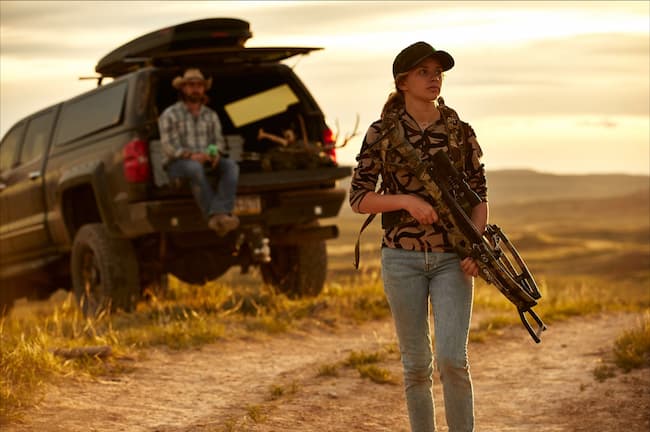 A young girl walking away with a crossbow to share the sport. 