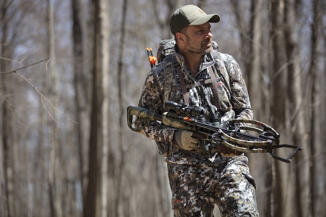 Bowhunter with crossbow and back quiver attached to his pack.