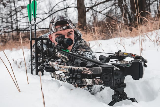bowhunter with ground quiver on crossbow setup laying in the snow ready to strike.
