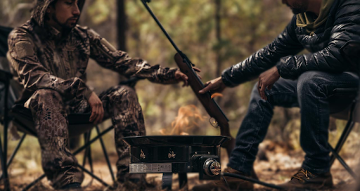 Pyramyd AIR, two campers sitting on either side of a firepit, one passing a break barrel air rifle to the other.