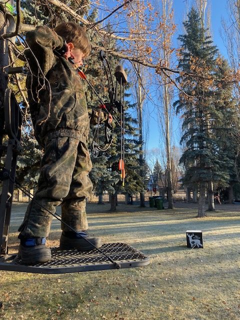 youth archer practicing on a tree stand with a cube target.