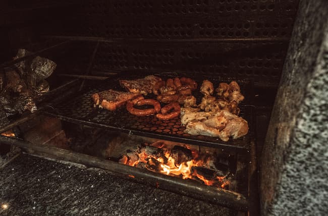 Grill full of meats cooking over a fire.