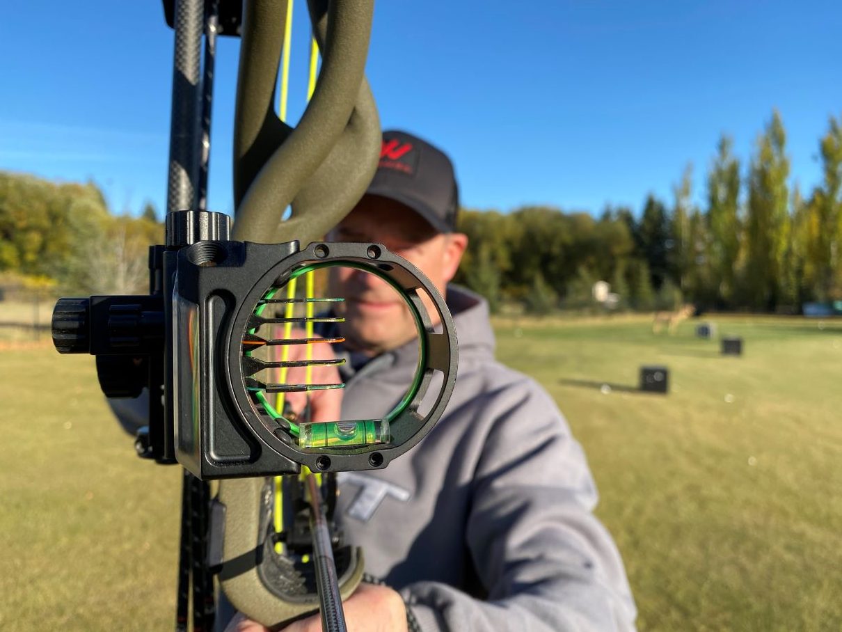 archer aiming his bow, the focus on the sight showing the pins.