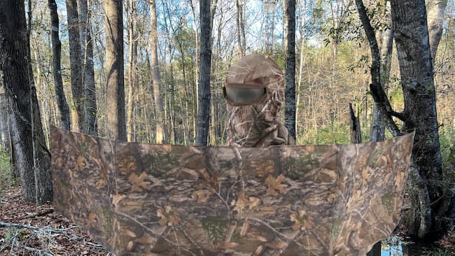 camouflaged hunter stationed behind hunting blind.