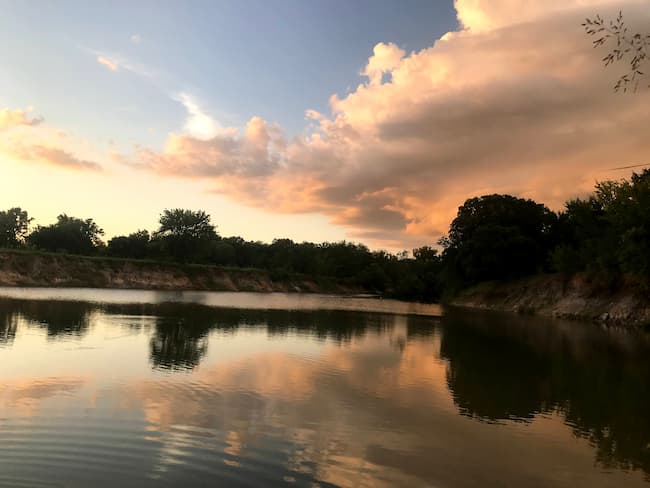 glistening lake at sunset rimmed by brush and trees.