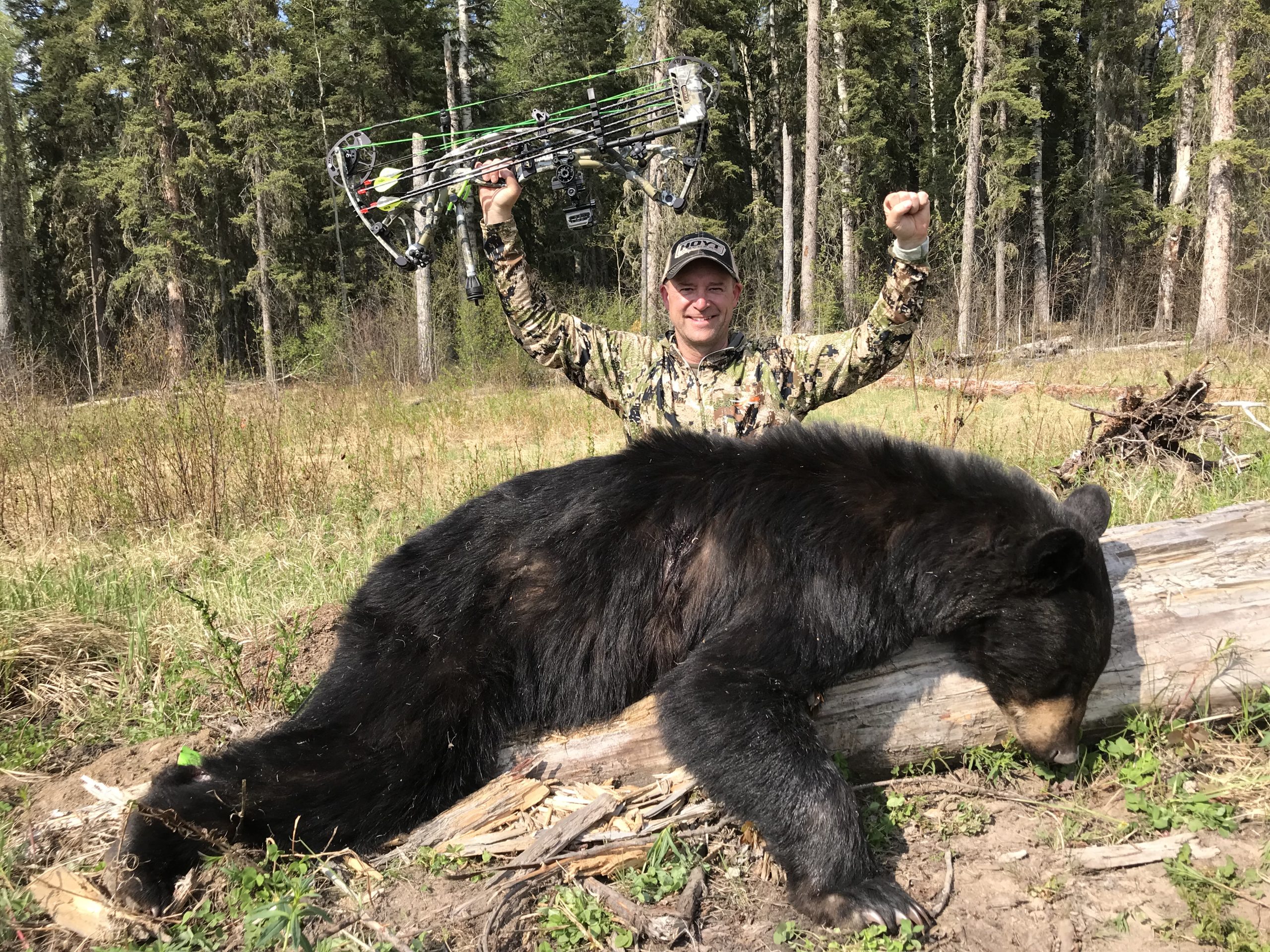 Kevin Wilson triumphant on bear bowhunting trip. author posing next to downed black bear.