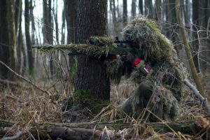 camouflaged hunter taking aim behind a tree