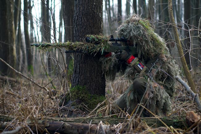 camouflaged hunter taking aim behind a tree