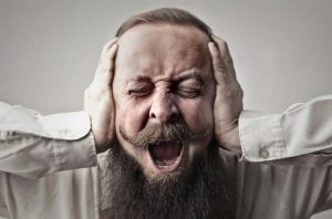 bearded and mustached man with hands over his ears yelling